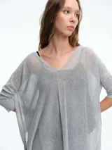 Sweater tipo túnica de tejido liviano con sutil transparencia y acabado brillante. Presenta escote en V, mangas largas relajadas y un corte amplio con largo asimétrico.