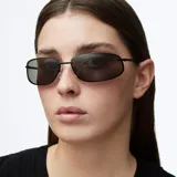 Lentes de sol con montura metálica negra y lentes rectangulares de cantos redondeados. Presentan un diseño envolvente inspirado en los años 2000 con patillas de acetato.