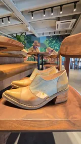 Zapatos de cuero color tostado con puntera fina y tacón bajo, estilo botineta destalonada con laterales abiertos y paneles elásticos en el empeine.