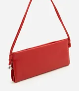 Bolso de mano tipo bowling en color rojo, de diseño alargado y estructura flexible. Presenta un acabado liso en poliuretano, con asa de hombro ajustable mediante nudos laterales y cierre magnético.
