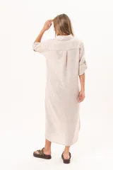 Vestido camisero largo de lino color beige, con silueta relajada, abotonado al frente, cuello camisero, mangas regulables y tajos laterales.