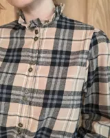 Camisa de algodón con estampado de rayas verticales finas, cuello alto con volados, cierre frontal con botones dobles y mangas largas con puños elásticos terminados en volados.