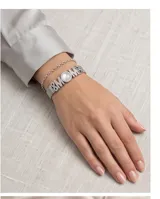 Pulsera de acero plateado con diseño de cadena tipo malla y dijes integrados que forman la palabra MOM, acompañados por un símbolo de infinito y corazones, con incrustaciones de cristales y una perla central.