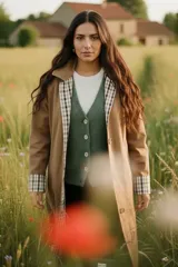 Trench reversible de corte clásico con cinturón ajustable. Un lado presenta un diseño liso en color verde militar, mientras que el reverso cuenta con un estampado a cuadros en tonos neutros. Posee cierre frontal con botones y cuello camisero.