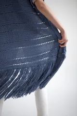 Chaleco largo de tejido de punto color azul verdoso, sin mangas y con flecos en el ruedo. Presenta calados con diseño geométrico.