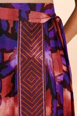 Falda tipo pareo de diseño envolvente con estampado de hojas en tonos púrpuras y cobrizos, con una franja lateral de patrón geométrico.
