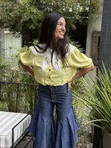 Camisa de lino amarillo claro, con mangas cortas abullonadas y un amplio cuello Peter Pan blanco con detalles bordados y calados. Cierre frontal con botones.