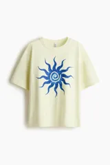 Remera oversized de algodón color amarillo claro con estampado frontal de sol azul. Presenta cuello redondo acanalado y mangas cortas con hombros caídos.