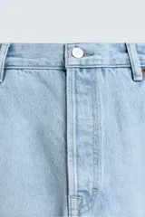 Jeans de denim de algodón, tiro medio, color celeste claro lavado. Corte recto y holgado desde la cadera hasta el tobillo, con rotura en una de las perneras. Presenta cierre frontal con cremallera y botón, y cinco bolsillos.