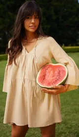 Vestido corto color beige, de lino y corte en A, con escote en V con tiras para anudar y mangas amplias.