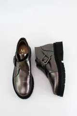 Botines de cuero metalizado en tono oscuro con acabado brillante. Presentan un diseño de corte bajo con una hebilla lateral decorativa y suela de goma negra con plataforma dentada.