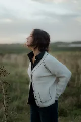 Saco tipo cardigan de punto color blanco con detalles de pespuntes decorativos en color negro a lo largo de los bordes y costuras. Presenta cuello en V, cierre frontal con botones y mangas largas.