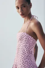 Vestido midi de color rosado con estampado de lunares negros, cuello halter con tirantes finos ajustables, escote recto y diseño fluido con volumen.