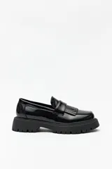 Mocasines tipo chunky de charol negro con detalle de flecos en el empeine y suela de plataforma dentada.