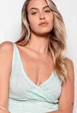 Top tejido color verde agua, sin mangas, con escote en V profundo y diseño cruzado en frente y espalda. Presenta calados y detalle de punto smock en la parte inferior.