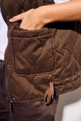 Chaleco reversible de algodón con acabado lavado y diseño acolchado con pespuntes ondulados. Presenta cuello alto con cordón ajustable, cierre frontal de cremallera y botones a presión, bolsillos delanteros tipo parche y cordón de ajuste en el bajo.