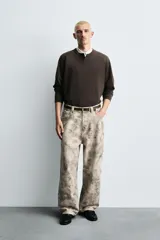 Pantalón de corte relajado confeccionado en algodón, con diseño de efecto lavado y estampado abstracto en tonos grises y beige. Presenta cinco bolsillos y cierre frontal con cremallera y botón.