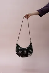 Bolso de hombro tipo hobo, confeccionado en gamuza color marrón oscuro, decorado con tachas metálicas plateadas en toda su superficie frontal. Cuenta con un asa corta fija y cierre superior.