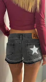 Short de jean negro con efecto lavado, de tiro bajo y corte ajustado. Presenta bordes deshilachados en el ruedo y una estrella blanca estampada en el bolsillo trasero derecho. Incluye etiqueta de cuero sintético en la parte posterior.