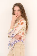 Blusa de manga tres cuartos color beige con estampado floral multicolor, escote en V y detalles de volados frontales junto a la botonadura.