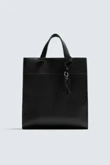 Bolso de hombro liso color negro, con cierre de imán en el compartimento principal y bolsillo interior con cremallera. Incluye un charm decorativo, dos asas de mano y un asa de hombro ajustable y extraíble.
