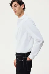 Camisa H&M de corte slim fit, color blanco, confeccionada en tejido elástico con cuello italiano y cierre frontal de botones.