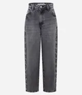 Pantalón baggy de jean color gris desteñido, con corte amplio y recto. Presenta una hilera de ojales metálicos decorativos a lo largo de los laterales y cierre frontal con botón y cremallera.