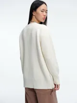 Sweater de tejido de punto acanalado en color blanco, con cuello redondo, mangas largas y corte holgado. Presenta un diseño minimalista y contemporáneo.