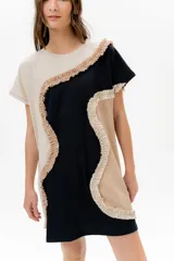 Vestido corto de algodón, con bloques de color en tonos pastel (amarillo claro, beige y rosado pálido) unidos por volados fruncidos en tonos marrón claro y amarillo. Presenta cuello redondo y mangas cortas.