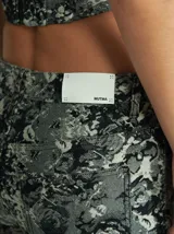 Pantalón de corte recto y tiro medio-alto, confeccionado en algodón grueso con apariencia de denim. Presenta un estampado abstracto en tonos grisáceos y negros, con bolsillos delanteros y traseros.