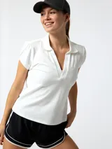 Remera polo de piqué color blanco, con manga corta abullonada, escote en V profundo y cuello clásico.