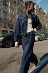 Chaqueta estilo bomber de Zara confeccionada en tejido denim azul oscuro. Presenta cuello solapa, cierre frontal con cremallera, bolsillos delanteros con solapa y bajo elástico que le otorga un ajuste ceñido en la cintura.