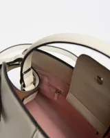 Cartera de mano color beige de diseño estructurado, con costuras verticales decorativas, manija superior y detalles de tiras con hebillas metálicas en los laterales. Incluye el logo de la marca en la parte inferior frontal.