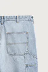 Pantalón jeans relaxed fit de mezclilla azul oscuro, con estilo carpintero que incluye bolsillos laterales y presillas de herramientas. Cuenta con costuras pespuntadas en contraste y cierre frontal con botón y cremallera.