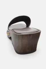 Sandalia de piel color marrón tipo zueco, con tira delantera ancha, detalle de tachas metálicas doradas en los laterales, tacón en bloque con efecto madera y puntera cuadrada.