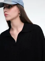 Sweater de tejido de punto color beige, con diseño de trenzas en el frente y mangas lisas. Presenta cuello polo con escote en V y puños y ruedo acanalados.