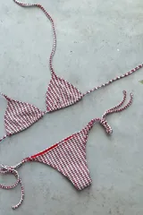 Conjunto de bikini con corpiño triangular de atar con apliques de argollitas y bombacha vedetina de atar con apliques de argollitas. El tejido presenta un estampado tie-dye o marmolado en tonos lila/azul y naranja/beige.