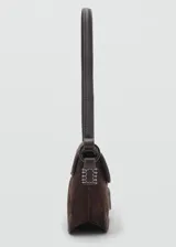 Bolso de hombro tipo baguette confeccionado en piel de serraje color marrón oscuro. Presenta un diseño rectangular con cierre de solapa y detalle metálico frontal. Incluye forro interior y bolsillo interno.
