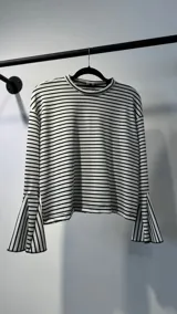 Remera de manga larga con diseño a rayas horizontales en blanco y negro. Presenta un corte holgado, cuello redondo y mangas acampanadas con abertura lateral.