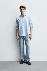Camisa de corte regular fit confeccionada en tejido de algodón con textura twill. Presenta cuello italiano, manga larga con puños abotonados y cierre frontal de botones.