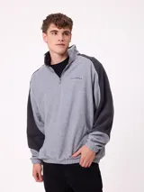 Buzo de polar con cierre frontal parcial, cuello alto y diseño de bloques de color en gris y negro. Presenta logo bordado en el pecho y puños elásticos.