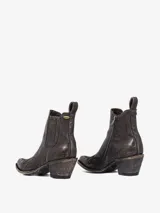 Bota corta estilo cowboy color marrón oscuro desgastado, con punta afilada y tacón ancho. Presenta elásticos laterales y costuras decorativas en el empeine.