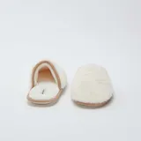 Pantuflas abiertas de pelo sintético color beige con suela marrón.