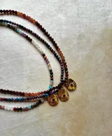 Collar de cuentas facetadas de piedras naturales multicolor con dije dorado ovalado en forma de sol con una piedra central.