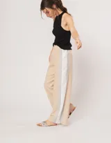 Pantalón palazzo color beige con cintura elastizada y dos franjas verticales en los laterales, una plateada y otra blanca.