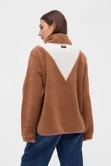 Buzo de sherpa color marrón con diseño de medio cierre frontal. Presenta un panel superior en forma de V en color beige y detalles de vivos en color fucsia en el cierre, cuello y bolsillos laterales. Cuenta con cuello alto y bolsillos frontales.