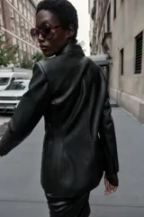 Blazer entallada de cuello solapa y manga larga con hombreras, confeccionada en efecto piel color negro. Cuenta con bolsillos delanteros con solapa y cierre frontal cruzado con botones.