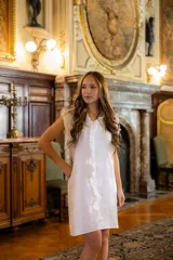 Vestido corto de lino en color blanco, con diseño sin mangas y volados verticales que recorren el frente. Presenta un corte recto y holgado con detalles de frunces en los hombros.