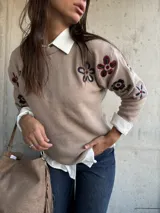 Sweater de punto color beige con cuello redondo y diseño de flores bordadas en tonos oscuros en el frente y las mangas.