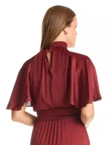 Vestido midi de satén color beige, con cuello alto fruncido, mangas cortas fluidas y cintura elástica tipo smock. Presenta una falda plisada con caída fluida y forro interno.